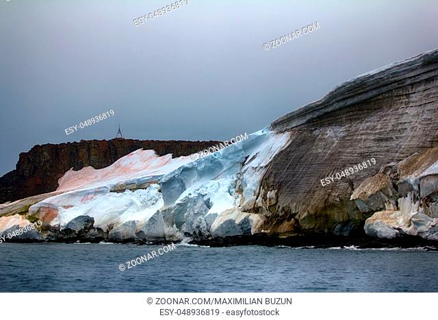 Harsh appeal of Arctic. Columnar rocks, cliffs, glaciers and snowfields Rudolf island, Franz-Joseph Land. Red spots and streaks on snow is colony of...