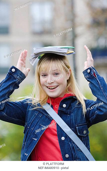 Portrait of smiling teenage girl holding books on head