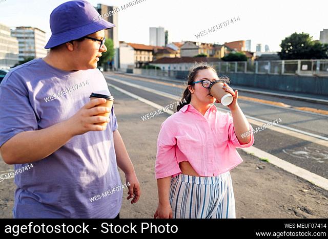 Teenage girl with down syndrome drinking coffee by brother on street in city