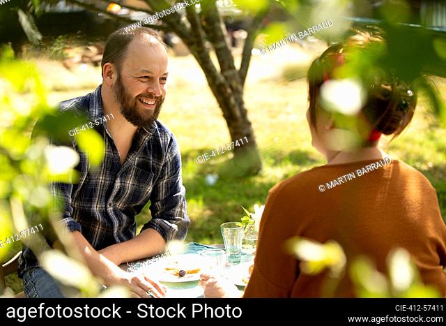 Happy couple enjoying cake at table in sunny summer garden