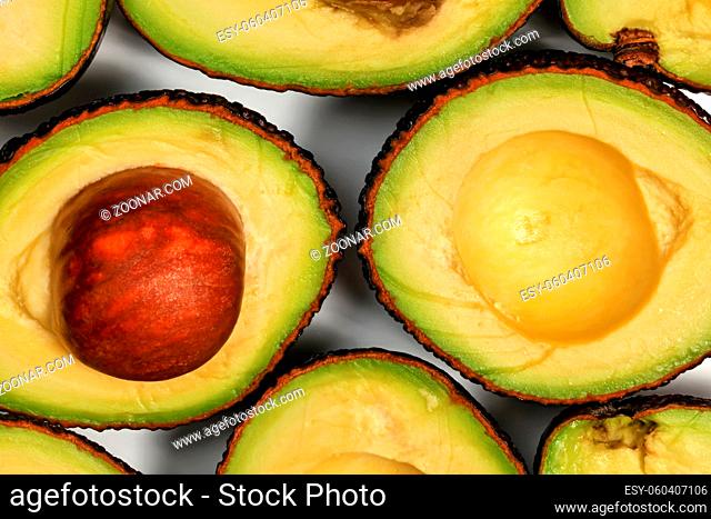 Avocado halves, one fruit with brown seed inside, arranged on white board, closeup macro detail