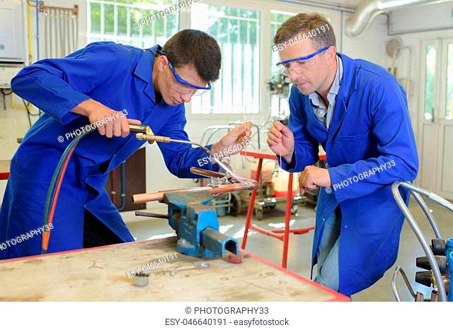 Instructor watching apprentice use blow torch