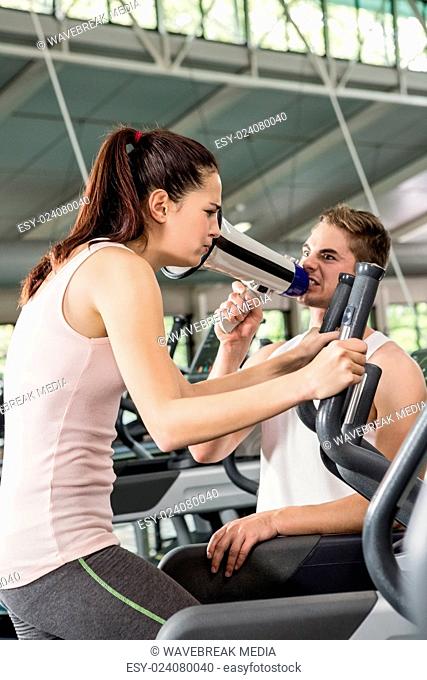 Trainer yelling through a megaphone while woman exercising on elliptical machine