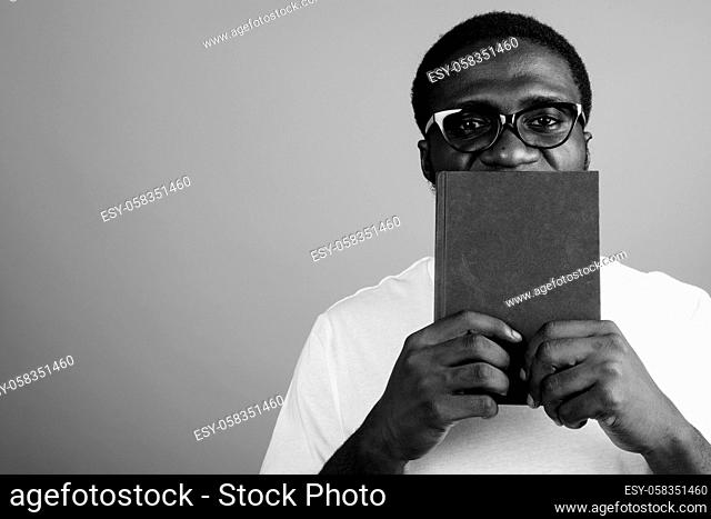 Studio shot of young African man wearing white shirt and eyeglasses against gray background in black and white