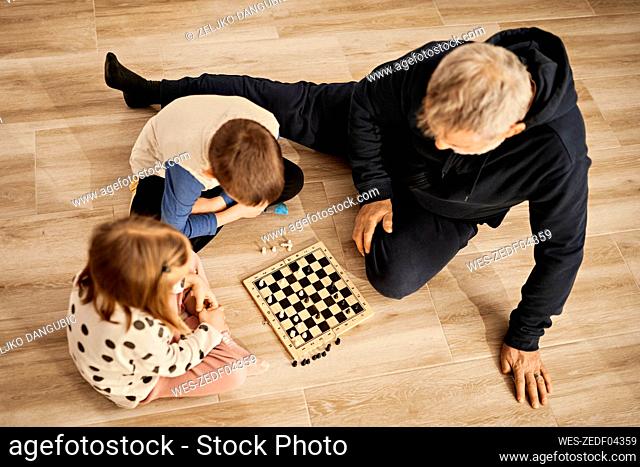 Sibling playing chess sitting with grandfather at home