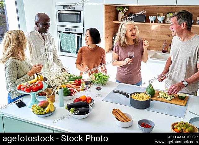 Diverse group of senior friends drinking wine while gathered at kitchen