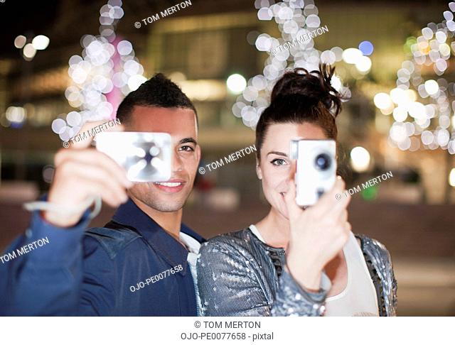 Couple taking pictures on city street at night