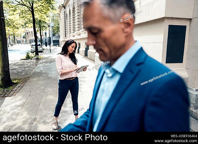 Businesswoman using tablet PC with mature businessman in foreground