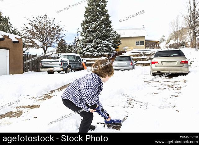 A six year old boy shoveling snow in driveway