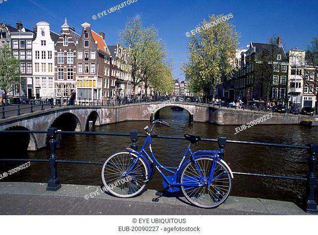 Blue bicycle leaning against a railing on bridge with Keizergracht Canal running parallel and Leidsegracht perpendicular
