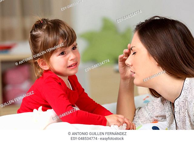 Fed up woman listening to her two years old daughter crying sitting on the bed in a house interior