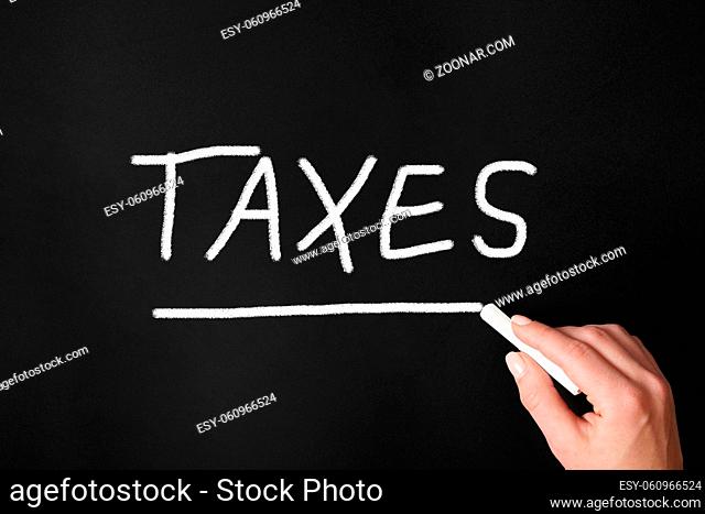 female hand writing word taxes with chalk on chalkboard or blackboard - tax concept
