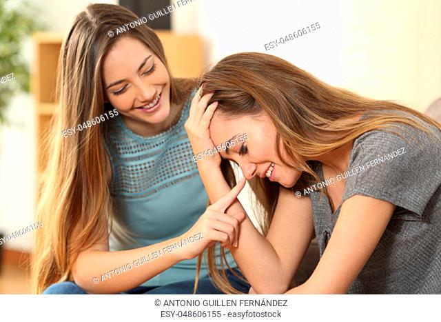 Girl trying to comfort and making laugh to her sad best friend after a bad day sitting on a couch in the living room at home