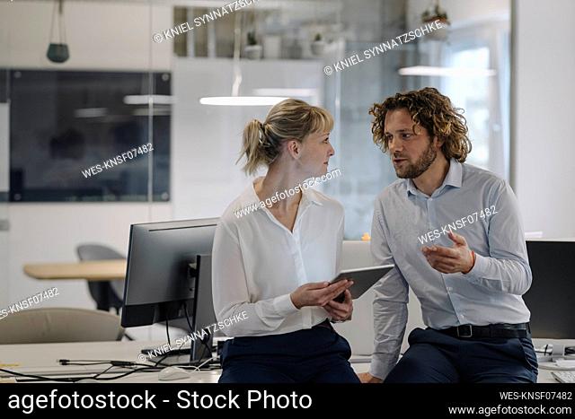 Businessman and businesswoman with tablet talking in offce