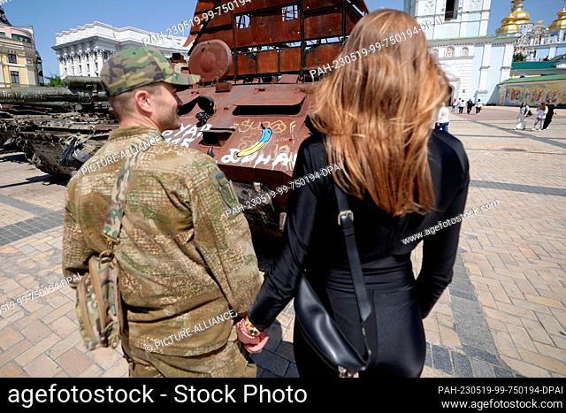 18 May 2023, Ukraine, Kiew: A young couple stands in front of a downed Russian tank, on which the Cologne artist and banana sprayer, Thomas Baumgärtel