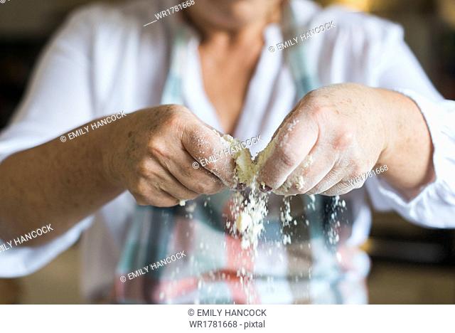 A woman crumbling and sifting white flour and butter, making a crumble topping. Home baking