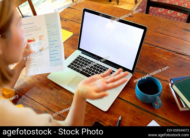 Asian woman on video call using laptop with blank screen, sitting at table, working from home