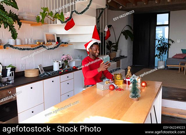 Happy african american man wearing santa hat, using smartphone for video call
