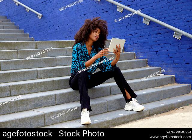 Afro woman using digital tablet while sitting on staircase
