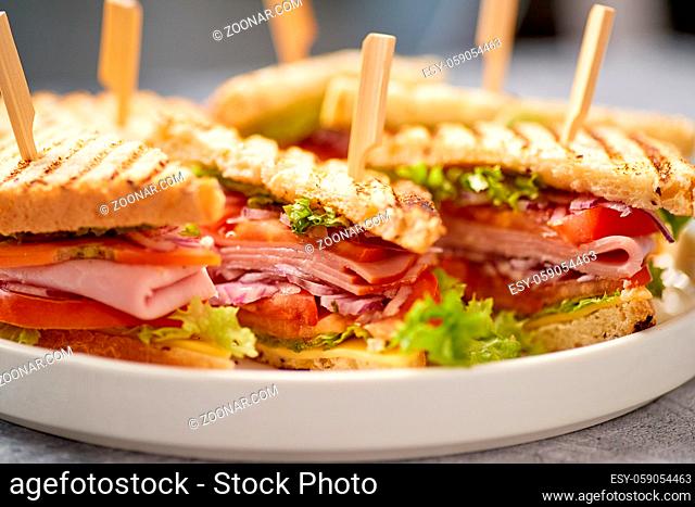 Close up on appetizing fresh and healthy grilled club sandwiches with ham, cheese, tomato and vegetables served on a metal tray. Fast food concept