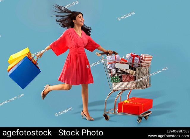 A young woman carrying colorful shoppingbags moving a cart full of gift boxes