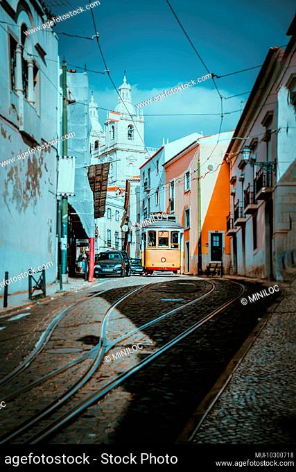 Summer cityscape of Lisboa. Red tram going down the hill along old traditional houses. sunny afternoon, narrow streets, cobblestones winding road