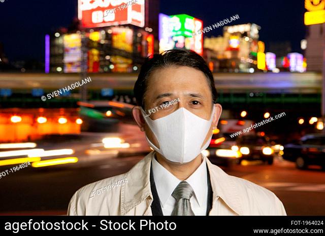 Portrait confident businessman in face mask in city at night, Tokyo, Japan