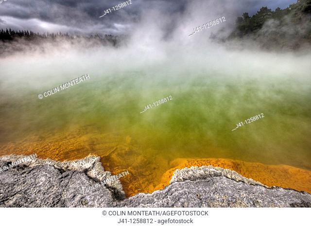 Champagne pool, burst of sunshine lights up foreshore during day of blowing mist and heavy rain, Wai-o-Tapu thermal region, Rotorua