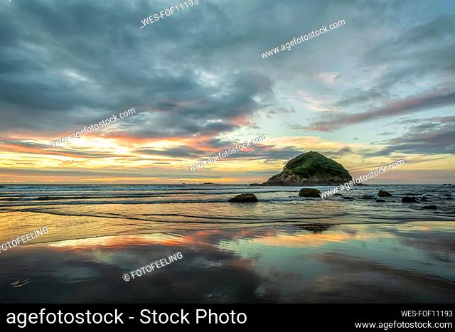 New Zealand, Tongaporutu, Cloudy sky over sandy coastal beach at dusk with Motuotamatea island in background