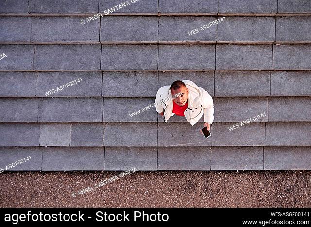 Young man holding smart phone while standing on steps