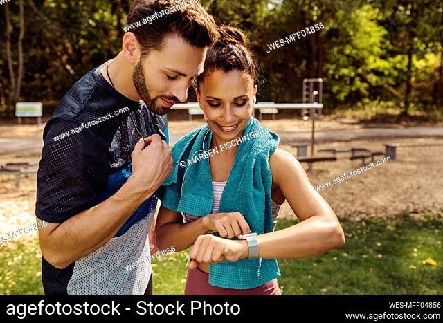 Sporty man and woman looking at a smartwatch in a park