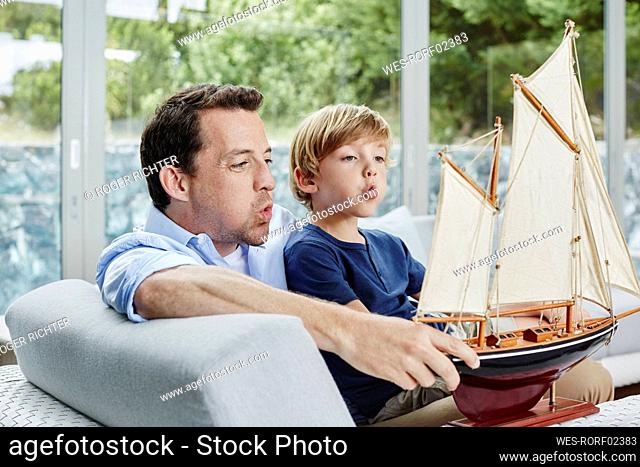 Father and son blowing toy boat while sitting at home