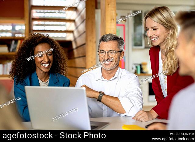 Smiling business people using laptop while working together in meeting at office