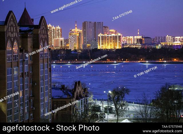 RUSSIA, BLAGOVESHCHENSK - FEBRUARY 25, 2023: A view of a tower block and the Amur River at dusk in winter. Seen in the distance is the Chinese city of Heihei
