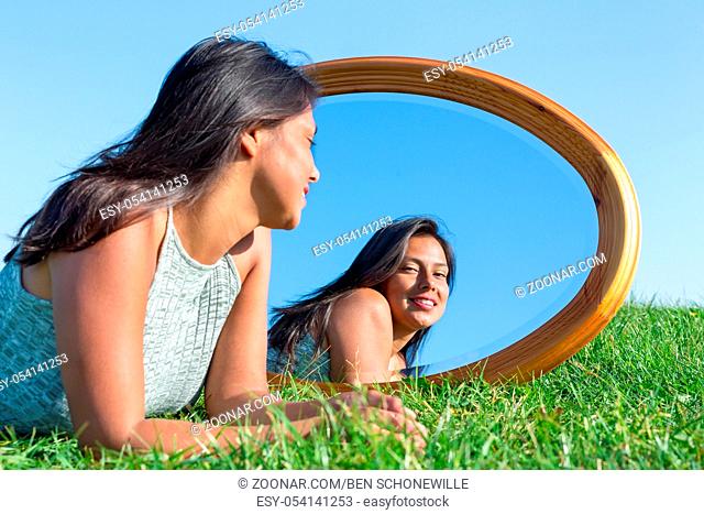 Woman lying on grass looking at her mirror image