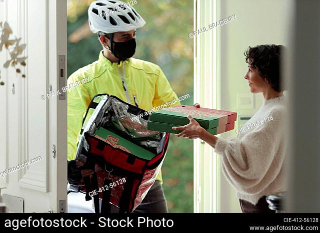 Woman receiving pizza delivery from courier in face mask at front door