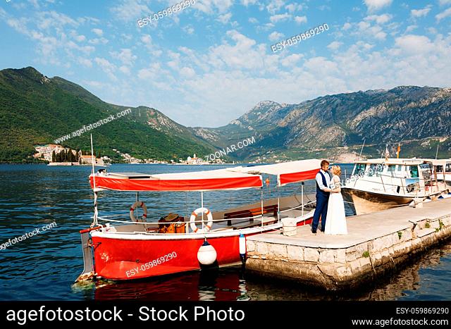 The bride and groom are embracing on the pier in the bay of Kotor, tourist boats near the pier . High quality photo