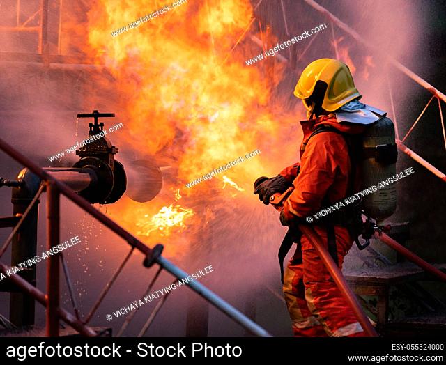 Firefighter using water fog type fire extinguisher to fighting with the fire flame from oil pipeline leak and explosion on oil rig and natural gas station