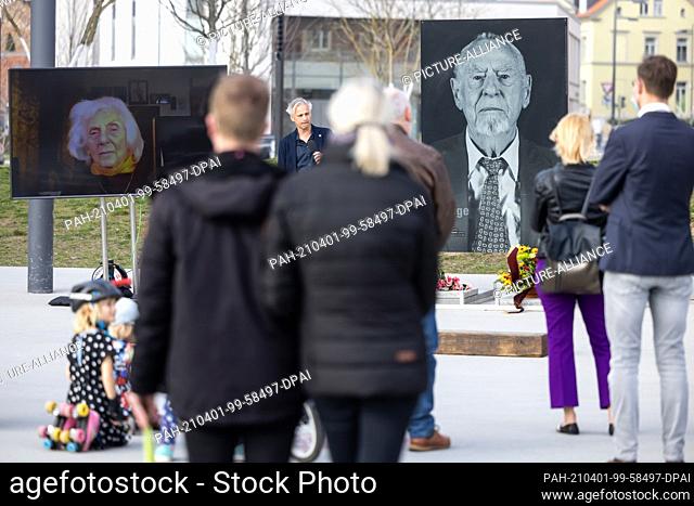 01 April 2021, Thuringia, Weimar: People stand during a minute's silence in front of the large portrait of Günter Pappenheim (r) on Stephane-Hessel-Platz