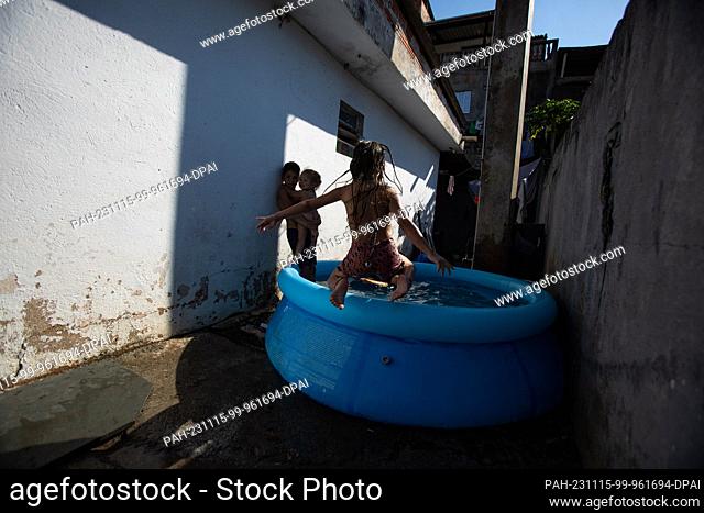 15 November 2023, Brazil, Sao Paulo: Children play in a small pool of water in a hallway during an extreme heatwave. Even before the start of summer in the...