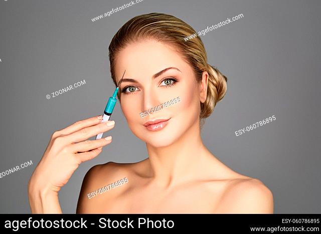 beautiful young woman holding syringe with collagen treatment injection. beauty shot on grey background. copy space