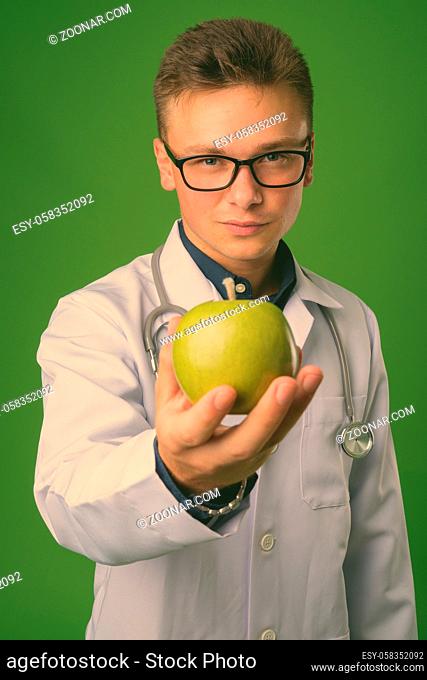 Studio shot of young handsome man doctor against green background