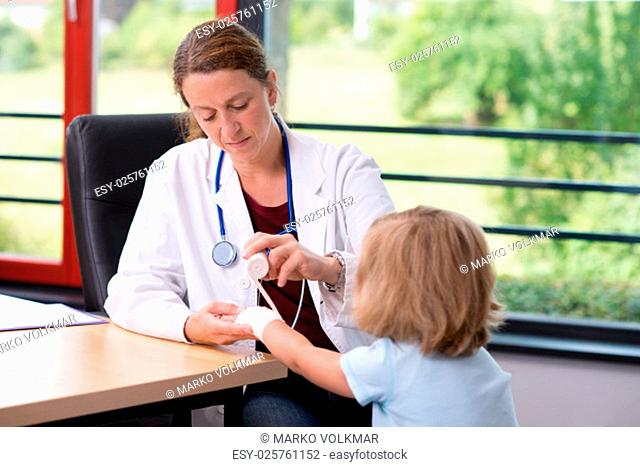 female pediatrician in white lab coat bandaging the arm of a little girl