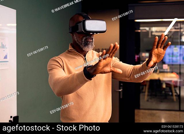 Mature african american businessman using virtual reality simulator gesturing at creative office