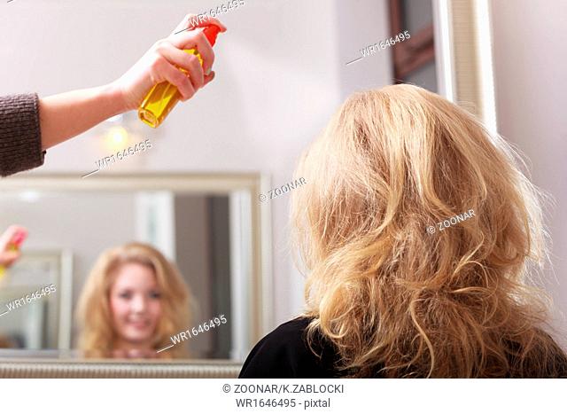 Girl with blond wavy hair by hairdresser. Hairstylist with hairspray and female client. Young woman in hairdressing beauty salon. Hairstyle