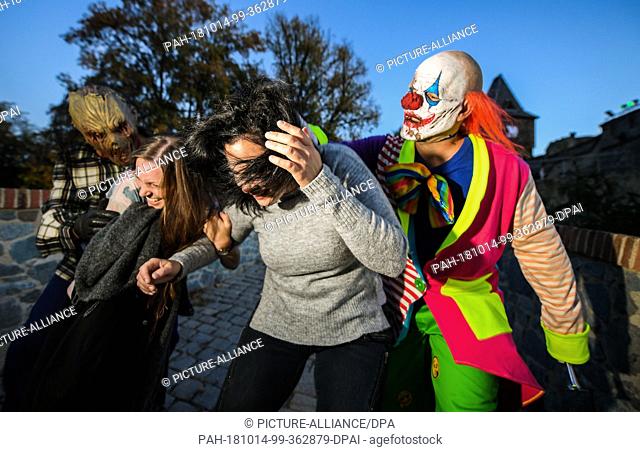 13 October 2018, Hessen, Muehltal: During the dress rehearsal, two visitors are followed by a horror clown and a scarred face