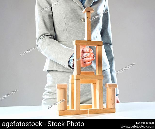 Business woman building tower on table from wooden blocks. Strategy planning and development concept. Young woman wearing formal wear sitting in office interior