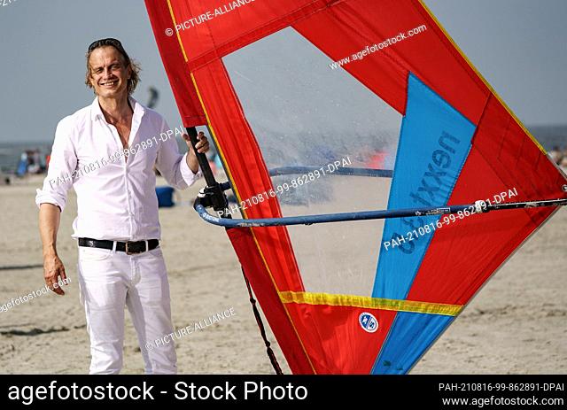 12 August 2021, Schleswig-Holstein, Sankt Peter-Ording: Actor Ralf Bauer stands on a surfboard on the beach of Sankt Peter-Ording