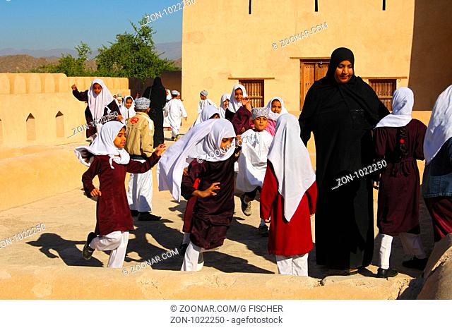 Erzieherin mit einer gemischten Schulklasse lebhafter Jungen und Mädchen beim Schulausflug im Fort von Nizwa, Sultanat Oman / Female teacher of a mixed school...