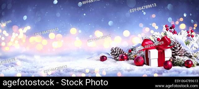 Gift Box On Snow With Bokeh Lights And Ornament In Fir Branch - Merry Christmas
